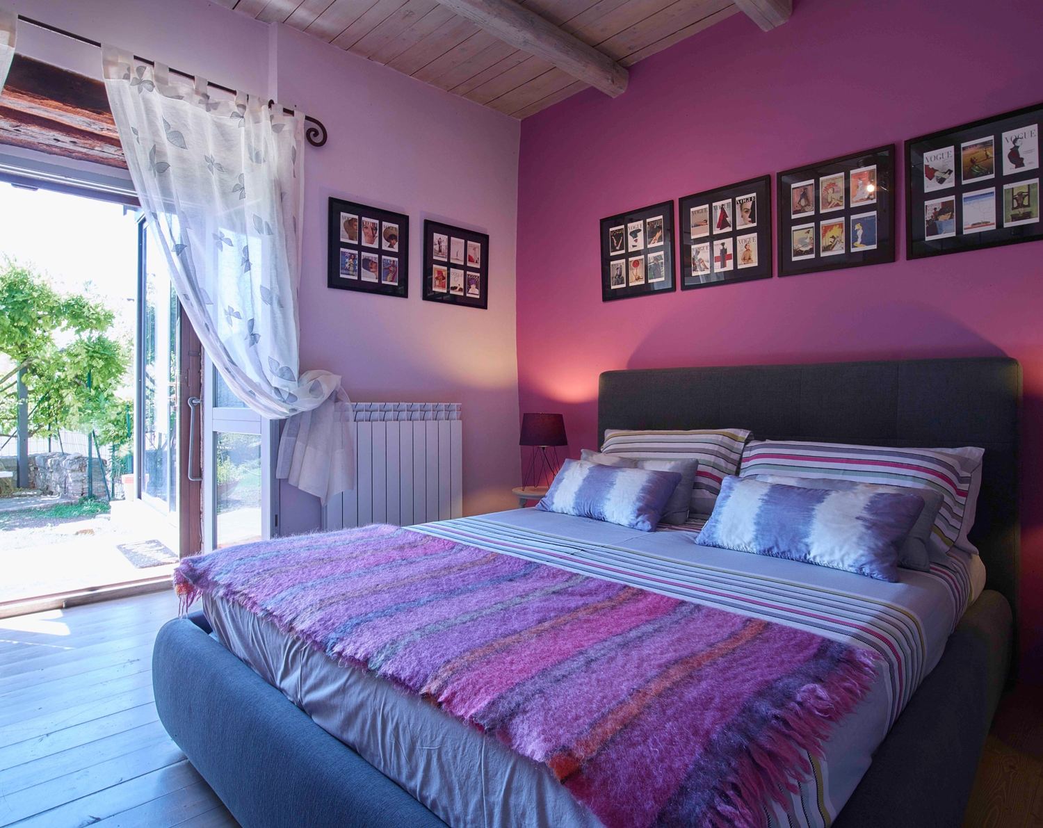King bedroom with a pink wall and doors open to the garden