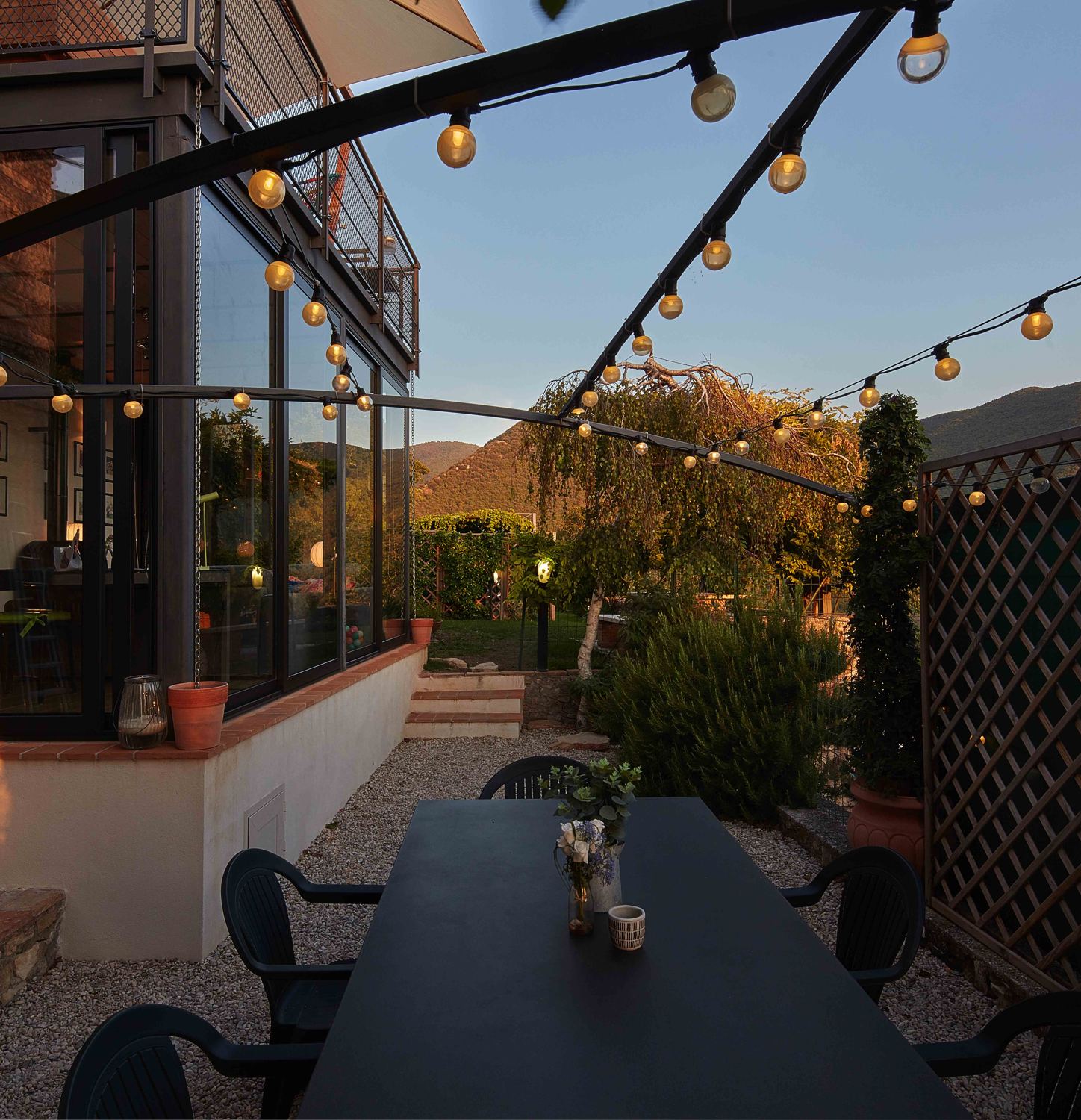 Garden dining table at dusk with festoon lights and the hills behind